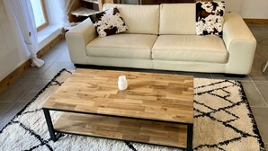 Ein Wohnzimmer mit einem beigefarbenen Sofa, zwei gemusterten Zierkissen, einem Holztisch und einem Teppich mit Muster.