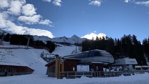 Schneebedeckte Berglandschaft mit Seilbahn, Holzbauten und einer Struktur mit Glasdach und Beschilderung.