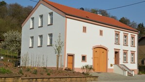 A two-story building with a red-tiled roof, a wooden door, and a small porch with steps. - Modern vacation apartment in a lovingly restored Lorraine farmhouse (Beckingen)
