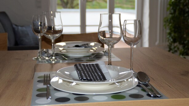 A dining table set with plates, cutlery, and wine glasses, with a view of greenery outside. - Modern vacation apartment in a lovingly restored Lorraine farmhouse (Beckingen)