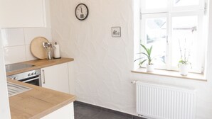 A kitchen with white cabinets, a wooden countertop, a clock, a radiator, and a window with potted plants. - Modern vacation apartment in a lovingly restored Lorraine farmhouse (Beckingen)
