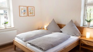 A double bed with checkered bedding, a wooden headboard, and two wall-mounted paintings. - Modern vacation apartment in a lovingly restored Lorraine farmhouse (Beckingen)