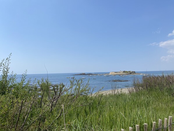 A coastal landscape with a clear sky, a sandy beach, and a small island with a building. - Renovated studio with sea view balcony, WIFI, near beach and shops - 2 pers (Ploemeur)