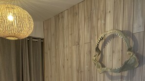A bedroom with a wooden wall, a bed with white bedding, a nightstand with a lamp, and a shark skull decoration.