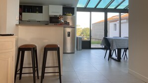 A modern kitchen with a large window, two stools, and a dining table with a striped tablecloth.