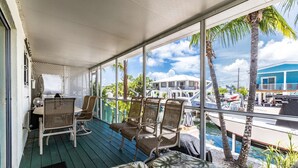 Un espacio exterior techado con mobiliario de mimbre y vistas al mar y edificios.