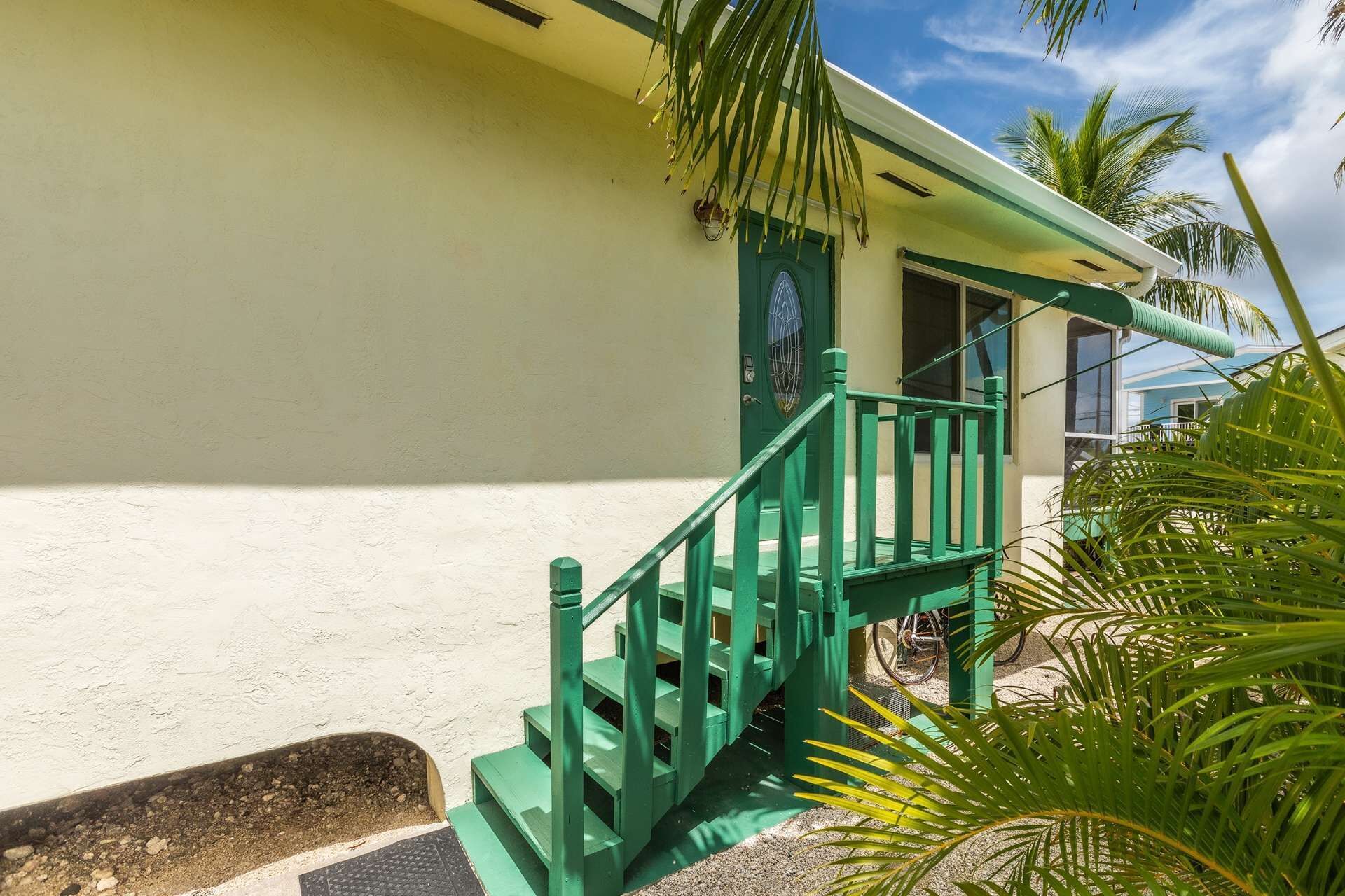 A building with a green staircase leading to a door, surrounded by palm trees.