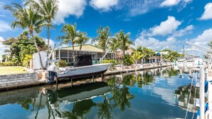 Puerto deportivo con un barco amarrado, palmeras y un edificio con zona cubierta.