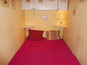 A small, single-bed room with a red bedspread, two pillows, a bedside table with a lamp, and a white cabinet above the bed. - Cozy studio for 6 at the foot of the slopes, Les Orres (Les Orres)