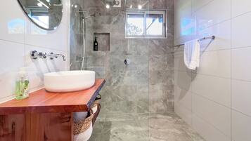 A modern bathroom with a glass shower enclosure, a wooden vanity, and a small window.