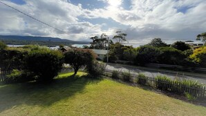 A grassy area with a wooden fence, trees, and a body of water in the background. - HEXAGON BEACH HOUSE - Great views of the Bay of Fires (Binalong Bay)