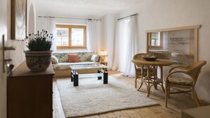 Un salon chaleureux avec un canapé, une table basse en verre, des fauteuils en osier, un tapis et une plante en pot.