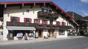 Un bâtiment traditionnel avec un magasin au rez-de-chaussée vendant des vêtements, un balcon orné de jardinières et une vue sur les montagnes en arrière-plan.