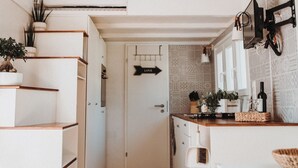 Une cuisine étroite avec des meubles blancs, un plan de travail en bois et un luminaire suspendu en fibres tressées.