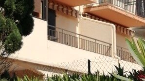Un edificio de varios pisos con balcones, una cerca de alambre y vegetación.