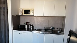 Cocina compacta con armarios blancos, un microondas, un tostador y un lavamanos.