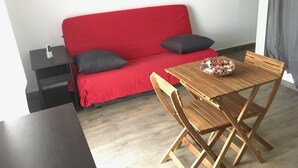 Una habitación pequeña con un sofá rojo, una mesa de madera y una silla.