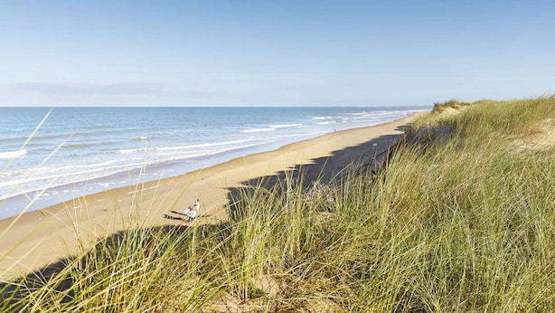 A beach with a clear sky, waves, and grassy dunes. - Spacious apartment for 4, balcony, sea view, near beach, parking, cleaning included (Saint-Hilaire-de-Riez)