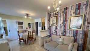 A living room with a beige sofa, a dining table with chairs, and a chandelier. - Spacious apartment for 4, balcony, sea view, near beach, parking, cleaning included (Saint-Hilaire-de-Riez)