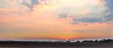 Solnedgang over et fladt landskab med en fjern horisont.