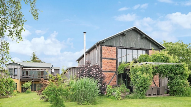Een rustiek gebouw met een bakstenen gedeelte en houten buitenkant, omgeven door een verzorgde tuin en een kleinere structuur met een balkon.