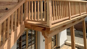 A wooden balcony with a railing, large windows, and a view of mountains.
