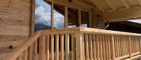 Un balcón de madera con barandilla, ventanas amplias y vista a las montañas.