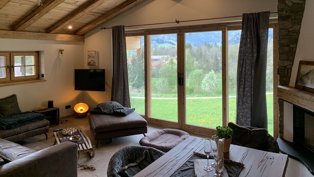 A cozy living room with a fireplace, a large window with curtains, a flat-screen TV, and comfortable seating.