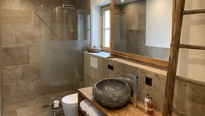 Ein modernes Badezimmer mit Duschkabine mit Steinplatten, einem großen Spiegel und einem Holzwaschtisch mit Steinbecken.