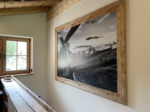 Een kamer met een groot zwart-wit fotokader van een berglandschap, een houten raam en een houten bank.