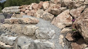 A rocky garden area with large stones and gravel, surrounded by trees and a building with a wooden roof.