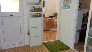 A room with a wooden floor, a white door, a small white cabinet, a green rug, and a painting on the wall. - Ferienhaus Waldoase für 2 - 3 Personen, Freistehend auf Eingezäuntem Grundstück (Beelitz)