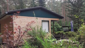 A small wooden cabin with a green roof, surrounded by dense forest. - Ferienhaus Waldoase für 2 - 3 Personen, Freistehend auf Eingezäuntem Grundstück (Beelitz)