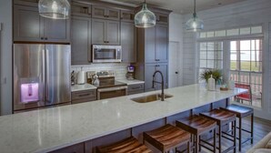 A modern kitchen with stainless steel appliances, a large island with bar stools, and pendant lighting. - Sweet Gum Cottage Oceanfront 5BDR with Golf Cart (Daufuskie Island)