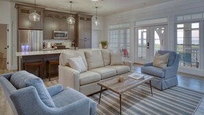 A spacious living area with a sofa, armchairs, and a coffee table. There is a kitchen with modern appliances and pendant lighting. - Sweet Gum Cottage Oceanfront 5BDR with Golf Cart (Daufuskie Island)