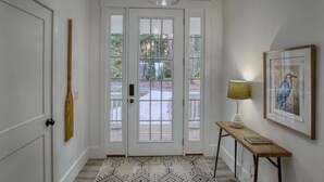 A hallway with a white door, a patterned rug, a table with a lamp, and a framed picture on the wall. - Sweet Gum Cottage Oceanfront 5BDR with Golf Cart (Daufuskie Island)