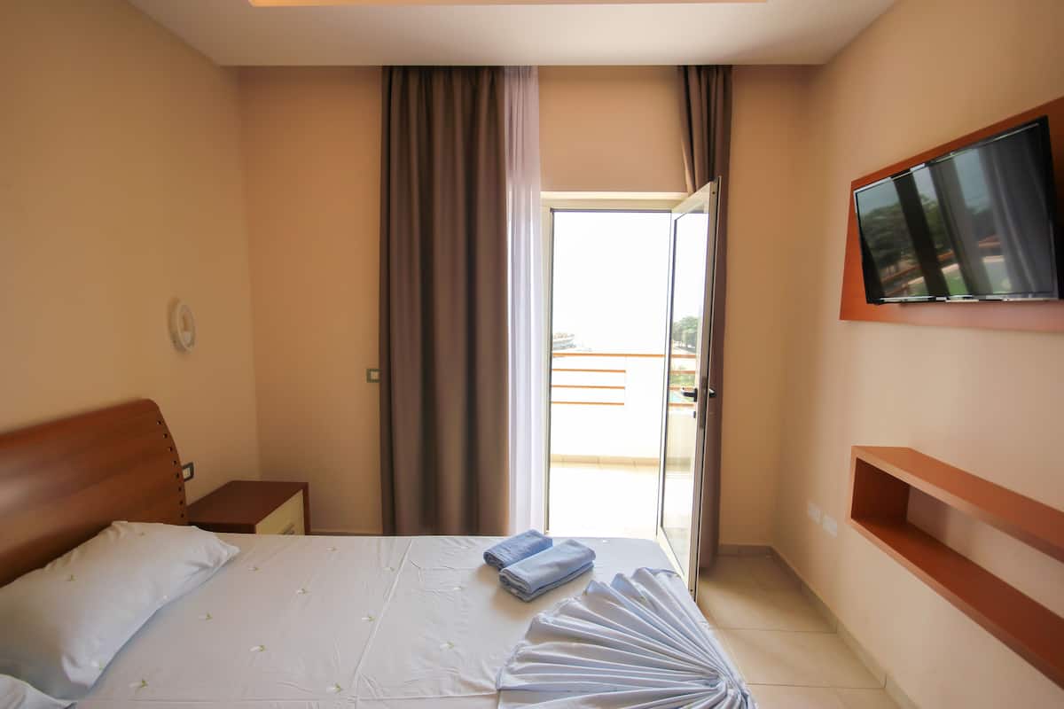 A hotel room with a bed, a TV mounted on the wall, a window with curtains, and a balcony.