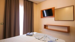 A hotel room with a bed, a flat-screen TV mounted on the wall, a window with curtains, and a bedside table with towels. - Ambassador Resort (Shengjin)