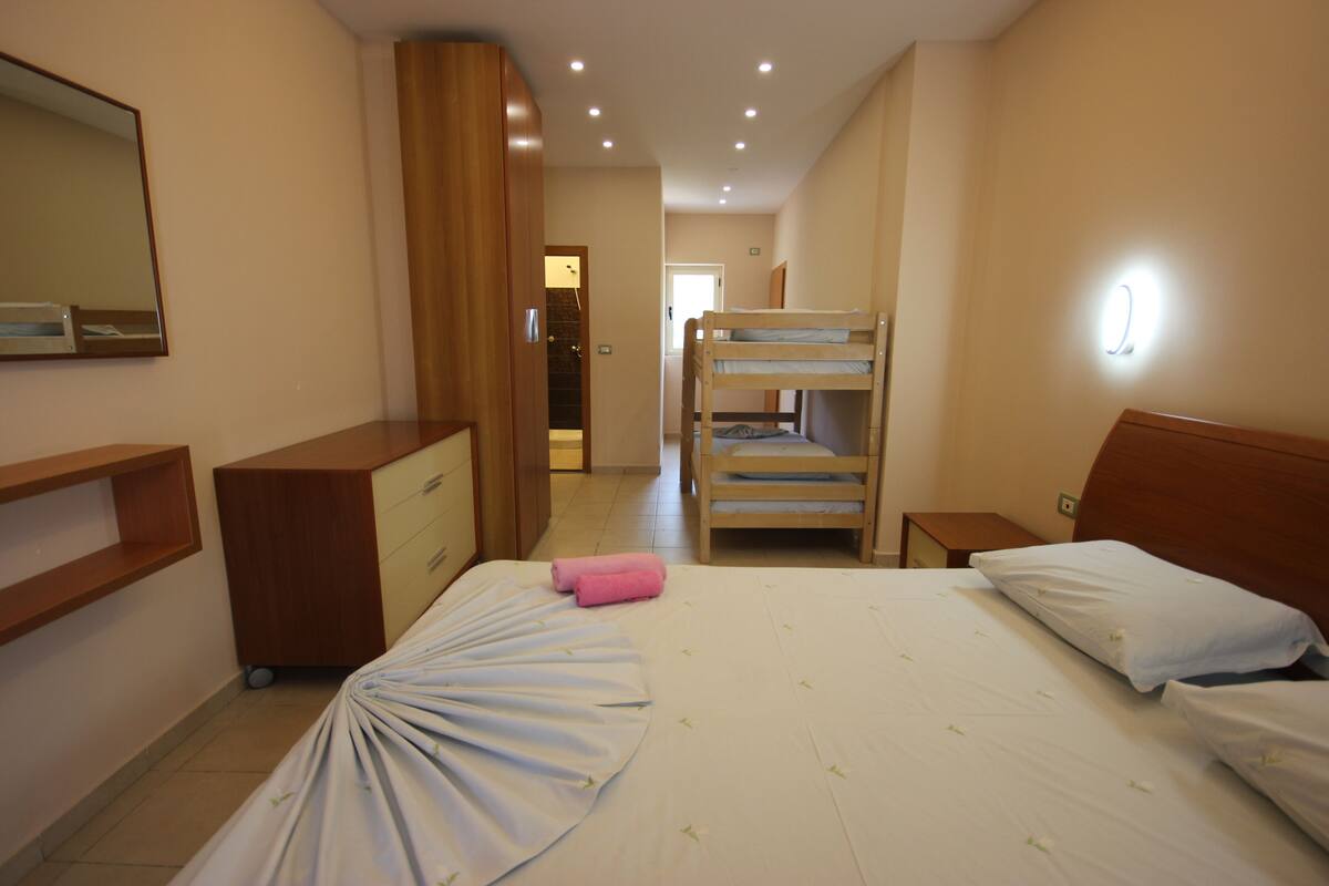 A hotel room with a bunk bed, a desk with a mirror, and a wooden wardrobe.