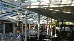 An outdoor cafe with tables and chairs, covered by a white pergola structure. - Ambassador Resort (Shengjin)