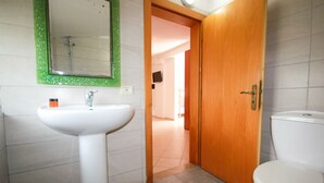 A bathroom with a white sink, a mirror with a green frame, a wooden door, and a white toilet. - Ambassador Resort (Shengjin)