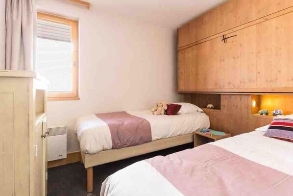 A bedroom with two beds, a wooden wardrobe, a radiator, and a window with curtains. - Belle Plagne Les Néreides 4* 2-room apartment 4/5 persons (Mâcot-la-Plagne)