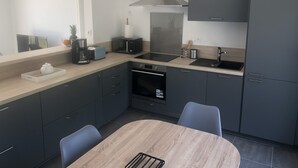 Een moderne keuken met donkere kastjes, een houten eettafel en een inbouwoven.
