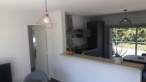 Een moderne keuken met een centraal eiland, een eethoek met tafel en stoelen, en een groot raam met uitzicht op de omgeving.