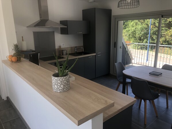 A modern kitchen with dark cabinets, a wooden countertop, and a dining area with a table and chairs.
