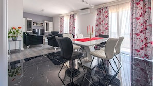 Un espace repas moderne avec un sol en marbre, une table à manger agrémentée d’un chemin de table rouge et des rideaux à motifs floraux.