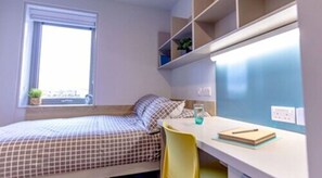 Un dormitorio con cama, escritorio, silla y ventana.
