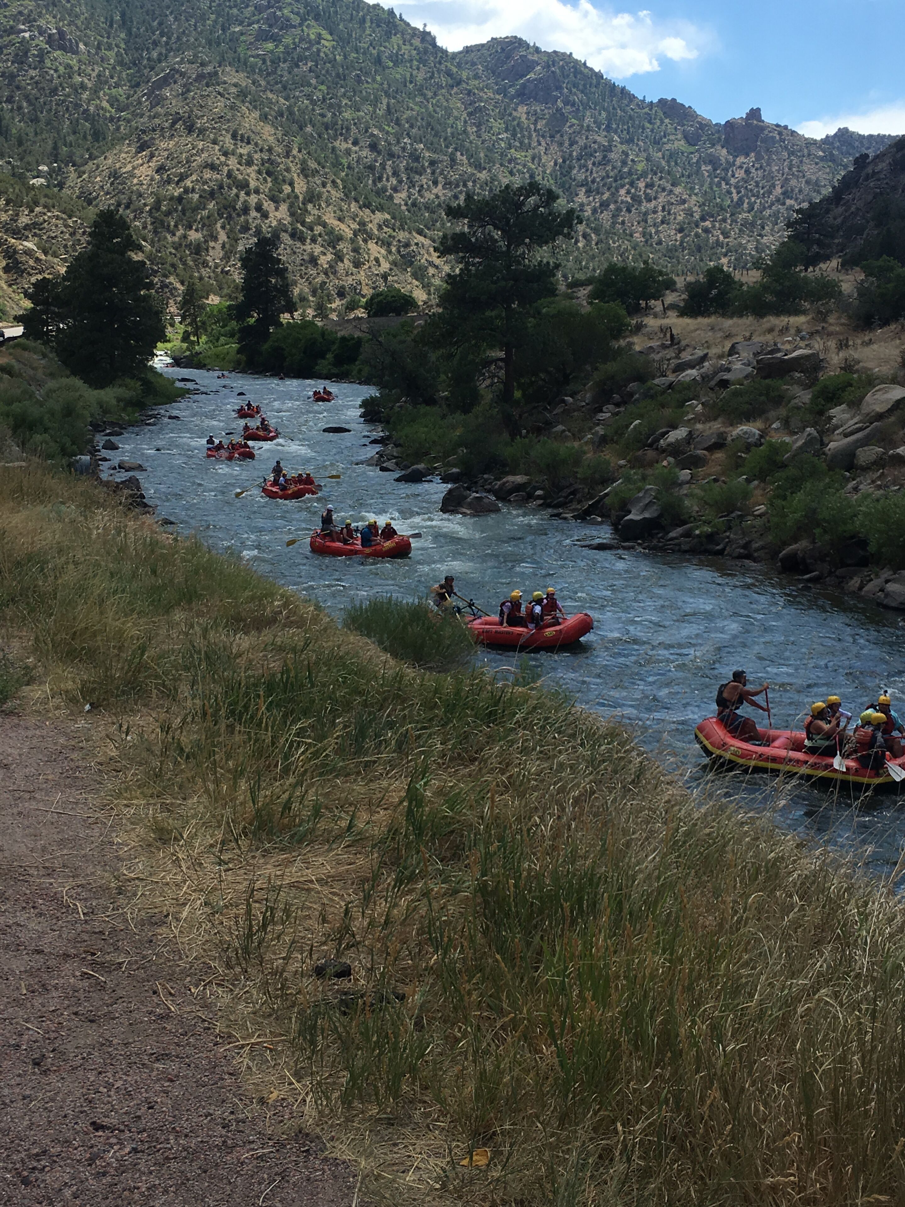 Une rivière où flottent de nombreux radeaux gonflables rouges, bordée de rives verdoyantes et dominée par un paysage montagneux.