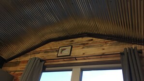 Una habitación con techo inclinado, vigas de madera, un cuadro enmarcado y una ventana con cortinas.