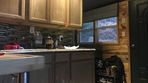 Una cocina con armarios de madera, salpicadero de azulejos y ventana con vistas a árboles.